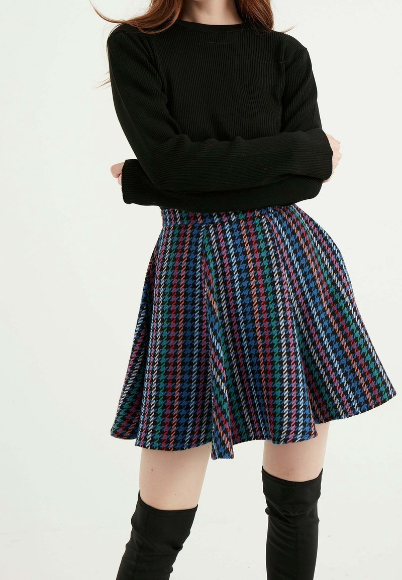 Černý žebrovaný top s dlouhým rukávem spárovaný s rozevlátou mini sukni s vícebarevným vzorem houndstooth v modré, červené, zelené a bílé barvě.