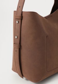 Brun lærveske med en glatt tekstur. Har en enkelt stropp med sølvfarget maskinvare og en sidelomme. Minimalistisk design.