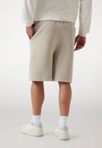Beige shorts with a relaxed fit, made from soft fabric. Features side pockets and a smooth waistband, paired with white sneakers and crew socks.