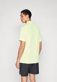 Polo vert clair à manches courtes avec un col, assorti à un short foncé. Texture lisse, coupe décontractée, avec des coutures sur les côtés.