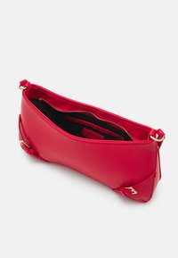 Červená kožená kabelka se zlatými přezkovými detaily, otevřený vršek ukazuje černý interiér a vnitřní kapsu na zip.