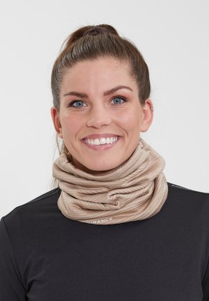 Beige rørformet halsedække lavet af blødt stof med ribbet tekstur. Båret over en sort langærmet top med et logo som accent.