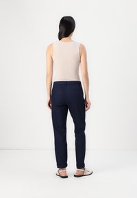 Granatowe, dopasowane spodnie garniturowe o gładkiej fakturze i z podwiniętymi nogawkami, zestawione z jasno-beżowym, bezrękawnym topem.
