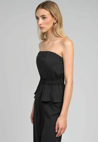 Top noir sans bretelles avec un col froncé et une taille peplum. Fabriqué en tissu lisse, mettant en valeur un design minimaliste et un éclat subtil.