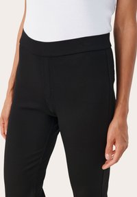 Zwarte broek van een gladde, elastische stof. Hoge tailleband en slank, tapere ontwerp. De zijnaad is subtiel gestikt voor een schone afwerking.