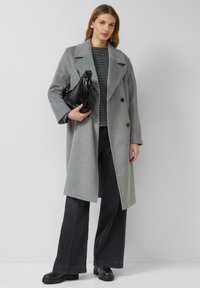 Szary wełniany płaszcz z dwurzędowym zapięciem, dużymi klapami, noszony na wzorzystej bluzce i zestawiony z szerokimi ciemnymi spodniami oraz czarnymi botkami.