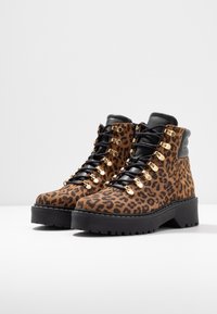Stivali alla caviglia con stampa leopardata, lacci neri, dettagli in oro e suola spessa nera. Realizzati in materiale texturizzato con un design robusto.
