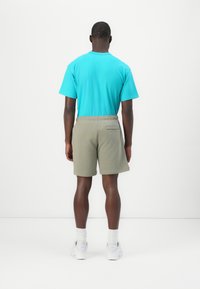 Tyrkist bomulls t-skjorte og olivenfargede shorts, elastisk midjebånd, baklomme på shortsen, brukt med hvite joggesko og sokker.