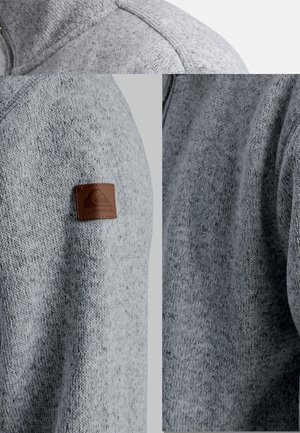 El suéter de punto gris presenta una tela texturizada, cuello alto y un parche de cuero marrón con el logotipo en el hombro izquierdo.