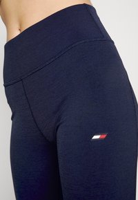 Marinblå yogabyxor med strukturerad tyg, hög midja och en liten logodetalj i röd, vit och blå på sömmen vid vänster lår.