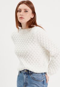 Pull en maille blanche présentant un motif de diamant texturé, un col côtelé et une coupe décontractée. Assorti à un jean taille haute bleu.