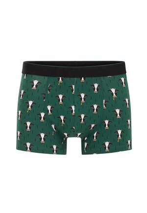 Boxers verts avec des visages de vache noirs et blancs répétés, portant une fleur jaune dans la bouche, et une ceinture noire.