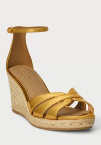 Zlatne kožne sandale na klin s prekriženim trakama, otvorenom prstiju i remenom oko gležnja; klin obložen jutom; glatka tekstura i minimalistički dizajn.