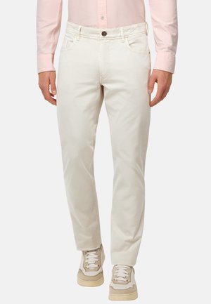 Pantalons en coton blancs avec une coupe droite, fermeture à bouton et design à cinq poches, associés à des baskets beiges. Texture lisse, sans motifs.