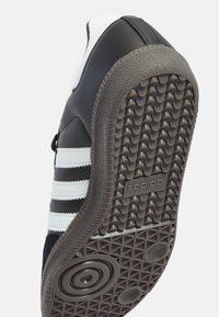 Zwart-witte Adidas sneaker gezien vanaf de zool, met een getextureerde rubberen buitenzool, het merklogo en drie witte strepen aan de zijkant.