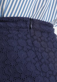 Mörkblå kjol med texturerad blommönstring och dragkedjestängning vid sidan, parat med en blå och vit randig topp.