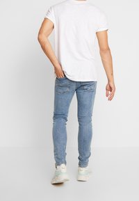 Jeans skinny de mezclilla azul claro con un acabado deslavado, con detalles de costura mínimos, combinados con una camiseta blanca y zapatillas blancas.