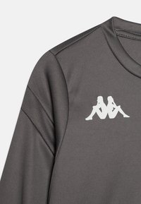 Pilkas sportinis marškinėlis su trumpomis rankovėmis, apvaliu iškirpte ir baltu logotipu, vaizduojančiu dvi sėdinčias figūras ant krūtinės. Lygi tekstūra.