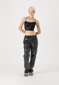 Top court en satin noir à fines bretelles, associé à un pantalon en sequins noirs brillants, avec une coupe ample et un design à jambes droites. Des sandales noires complètent le look.