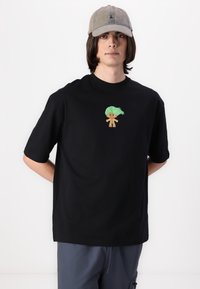 Black cotton t-shirt featuring a cartoon character with green hair on the chest; paired with a gray baseball cap.