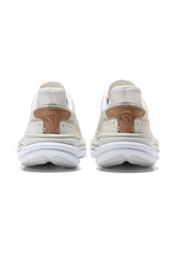 Par av vita sneakers med beige läderhälla, perforerade detaljer och tjocka vita dämpade sulor, sedda bakifrån mot en vit bakgrund.
