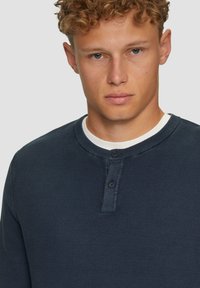 Granatowa, teksturowana koszula henley z okrągłym dekoltem, wyposażona w trzy guziki oraz kontrastującą białą kołnierzykiem.