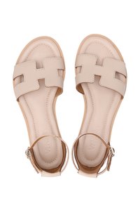 Helle beigefarbene Ledersandalen mit zwei breiten Riemen, einer Schnalle am Knöchel und einem glatten, minimalistischem Design. Flache Sohle mit strukturiertem Innenbereich.