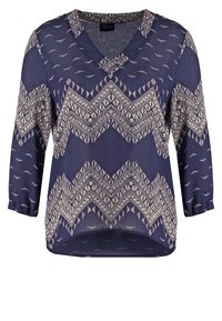 Blouse bleu marine à col en V avec motifs géométriques en zigzag et feuilles beige, manches trois-quarts, et ourlet légèrement arrondi.