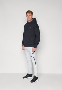 Dunkelblaues Kapuzensweatshirt mit Fronttasche und gerippten Bündchen, kombiniert mit hellgrauen tapered Jogginghosen mit schwarzen seitlichen Akzenten. Schwarze Sneakers.