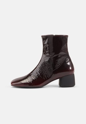 Burgundy patent leather nilkkurit, joissa on terävä kärki, vetoketjusulku ja keskipitkä tolppakorko. Sujuva, kiiltävä pinta, tyylikäs muotoilu.