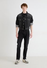 Crna traper jakna s dva džepa na prsima i srebrnim dugmadima, uparena s crnim trapericama i tenisicama s bež detaljima. Ugodne teksture kroz cijeli outfit.