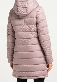 Manteau matelassé rose clair avec design à côtes horizontales, capuche attachée et manches longues. Texture douce et lisse, atteignant la longueur mi-cuisse.