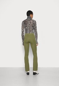 Top de gola alta com padrão de leopardo emparelhado com calças verdes justas; ambos apresentam mangas longas e uma textura suave. Sapatos pretos de salto completam o conjunto.