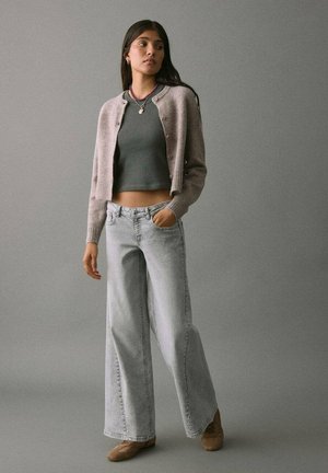 Un cardigan court gris clair sur un haut ajusté gris foncé, associé à un jean en denim bleu clair à jambes larges. Textures douces, design minimal, coupe décontractée.