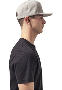 Hallide baseball müts, millel on lame ääre, valmistatud tekstuuritud kangast, koos tavalise musta T-särgiga. Profiilvaade, kus näo detaile on minimaalselt.
