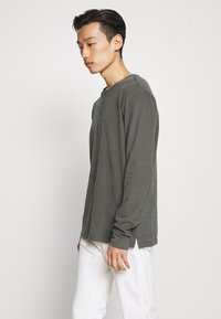 Tumerohelisest pehmest kangast pikkade varrukatega henley-särk, millel on ümar kaelus ja kolme nupuga klapiga. Äärte juures külgedel lõhikud.