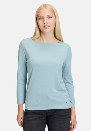 Hellblaues Langarmoberteil mit Rundhalsausschnitt und taillierter Passform. Der Stoff wirkt glatt mit minimalen Nähten und einem kleinen Logoakzent am Saum.