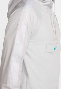 Lichtgrijze hoodie gemaakt van een gladde stof. Voorzien van een frontzak en een klein turquoise Nike-logo. Gestructureerde witte strepen op de mouwen.