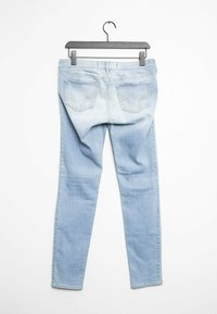 Ljust blå denimjeans, smal passform, midja i normalhöjd, med två bakfickor med sömnadsdetaljer, slät textur, hängande på en svart galge.