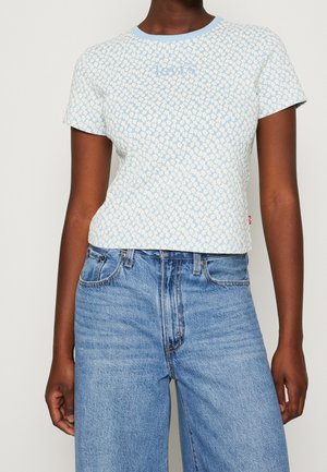 Woman wearing a light blue floral patterned short-sleeve top paired with high-waisted light blue denim jeans.