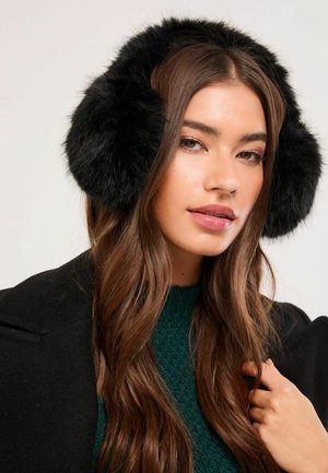 Black faux fur earmuffs with round, fluffy design and soft texture. Worn with a dark coat and textured dark green sweater.
