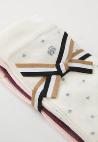 Set von Socken in verschiedenen Farben: weiß mit silbernen Punkten, pink und dunkelpurpur, gebunden mit einem schwarzen, weißen und braunen Band in einer Schleife.