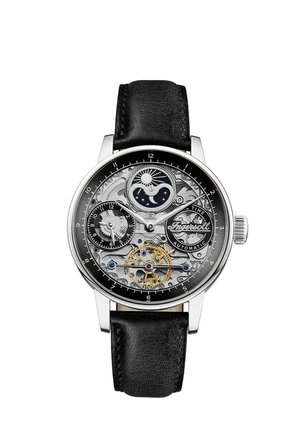 Montre mécanique avec un bracelet en cuir noir, boîtier en argent et un cadran transparent révélant des engrenages complexes et un indicateur de phase lunaire.