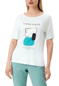 Lichtblauw graphic t-shirt met abstracte vormen in teal, zwart en wit. Korte mouwen en ronde hals. Tekst "UNIEKHEID" boven het ontwerp.
