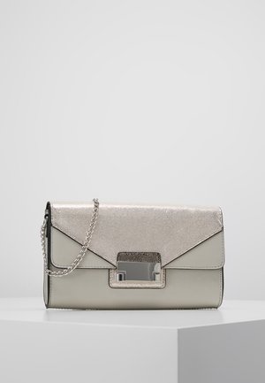 Pequeño bolso de mano rectangular plateado con solapa metálica, cierre rectangular y correa de cadena descansando sobre una superficie blanca.