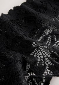 Tissu en dentelle noire avec des motifs floraux et géométriques, présentant un travail ajouré complexe et une surface texturée.