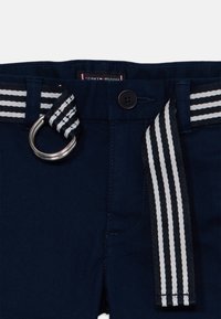 Pantalon bleu marine avec ceinture en tissu rayé noir et blanc, dotée d'une boucle double anneau argentée et d'une fermeture à bouton.