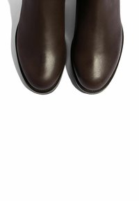 Botas de tobillo de cuero marrón con una superficie lisa y brillante y punteras redondas, con costuras mínimas y una suela plana.