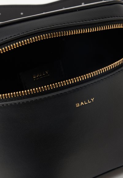 Μαύρη δερμάτινη τσάντα Bally με χρυστό φερμουάρ μερικώς ανοιχτό, εμφανίζοντας την εσωτερική ετικέτα και το χρυσό λογότυπο Bally εξωτερικά.
