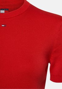 Maglietta rossa a maniche corte a coste, realizzata in cotone con scollo rotondo. Presenta un piccolo logo ricamato in blu, bianco e rosso vicino al colletto.